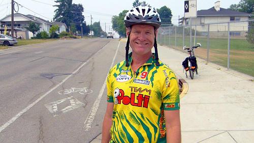 Rick August standing in front of a bicycle lane wearing his riding gear and helmet.